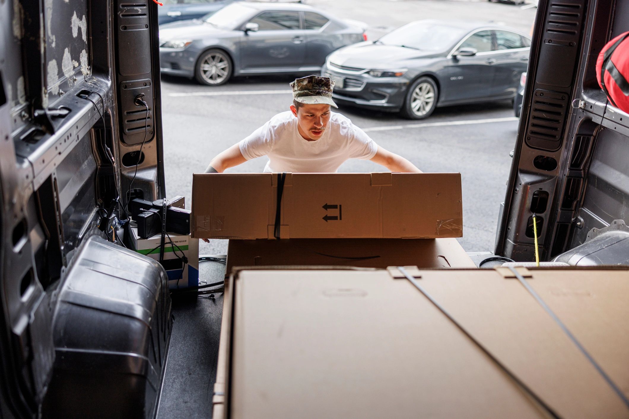 Cargo van unloading. Hispanic Navy officer carrying heavy boxes from the cargo van